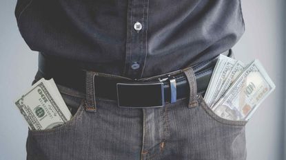 A man has stacks of $100 bills sticking out of both pants pockets.