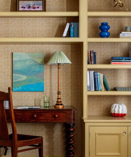Yellow bookshelf with ornaments and books, wooden desk and chair and vintage lamp