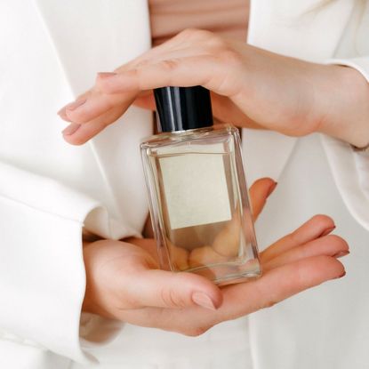 Woman in a white suit holding a perfume between her hands