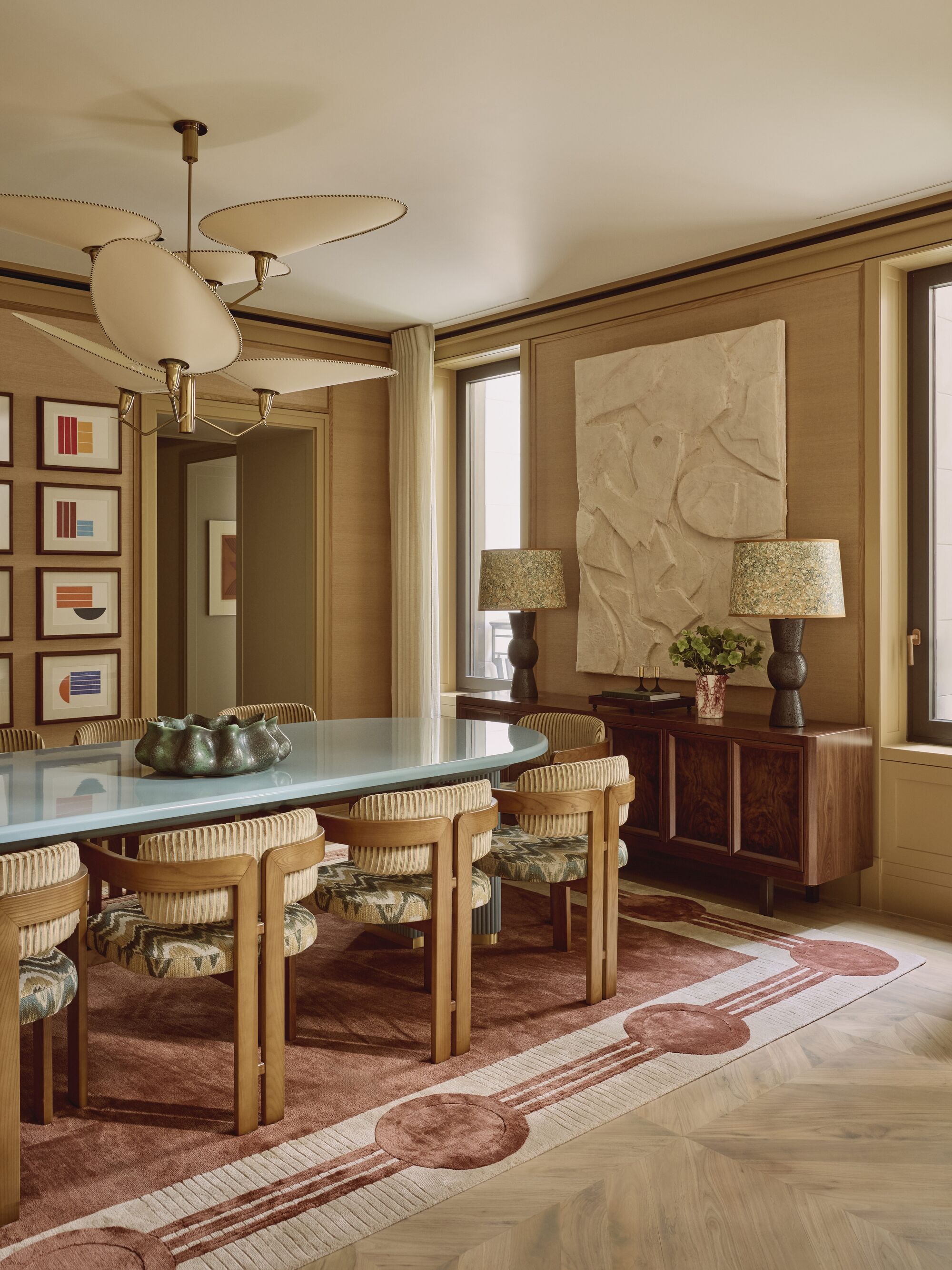 mid-century modern style dining room with rug, upholstered chairs, light blue table, statement pendant light, grasscloth walls, artwork and console styled with lamps