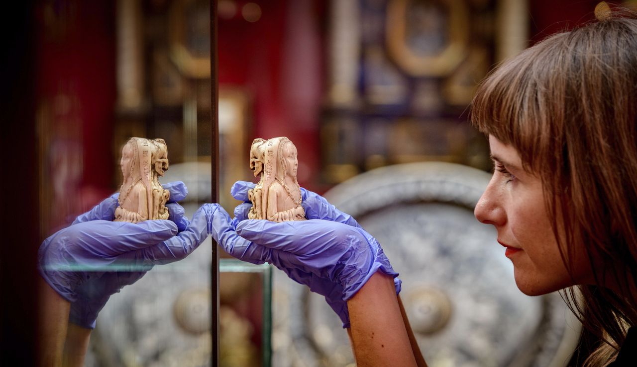 A curator with a small ivory pendant produced in the Netherlands in about 1500. Known as an example of a memento mori, or ‘remember death’ in Latin, this piece shows the two sides of human existence, juxtaposing life and death, in a gruesome way, to remind its owner to live a life free of sin. Photographed at Ranger&#039;s House in Greenwich, the home of the Wernher Collection.