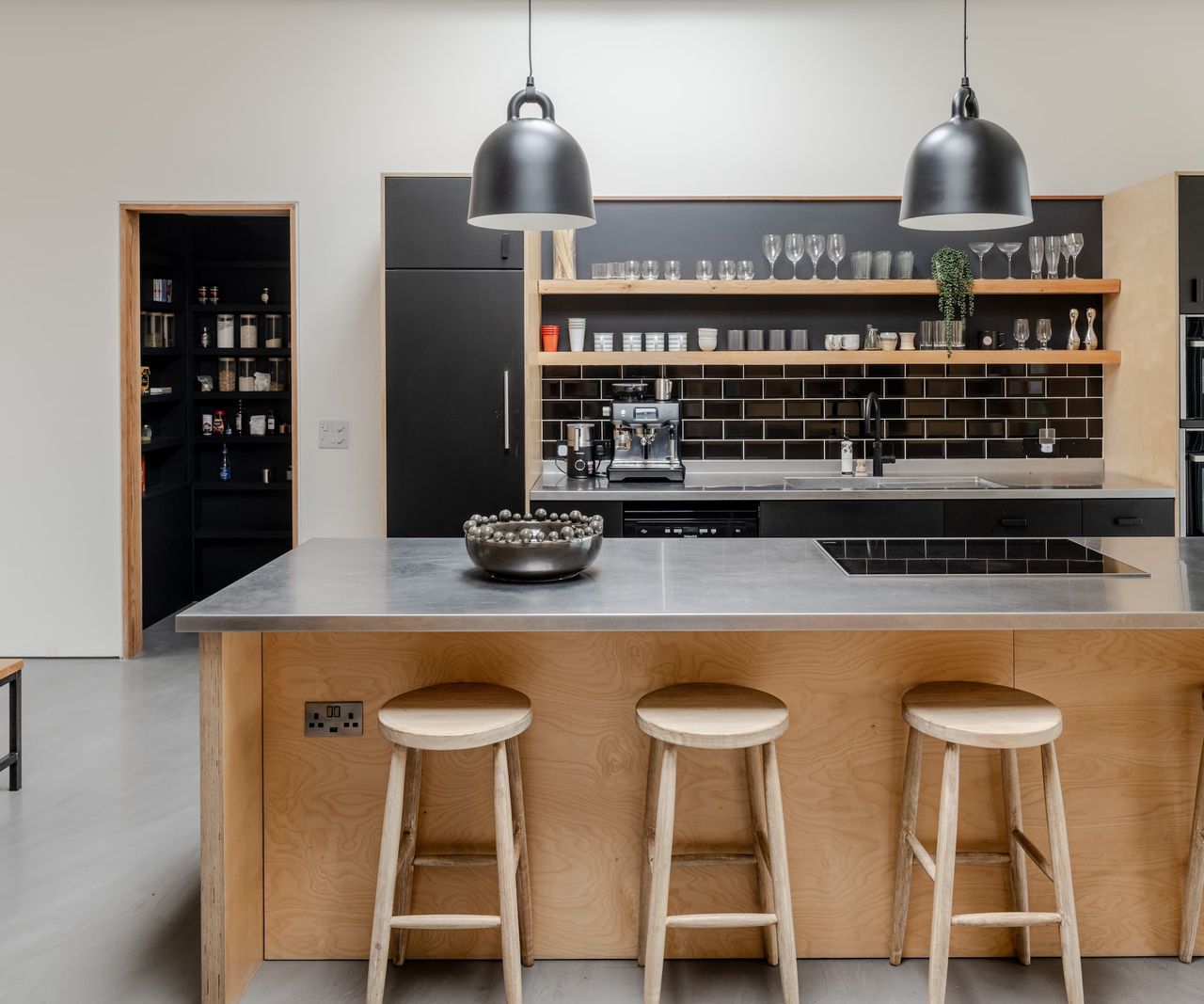 A kitchen island with wooden stools and a kitchen cooking area with a integrated pantry