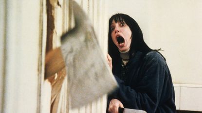 shelley duvall screams as an ax comes through a door in the shining