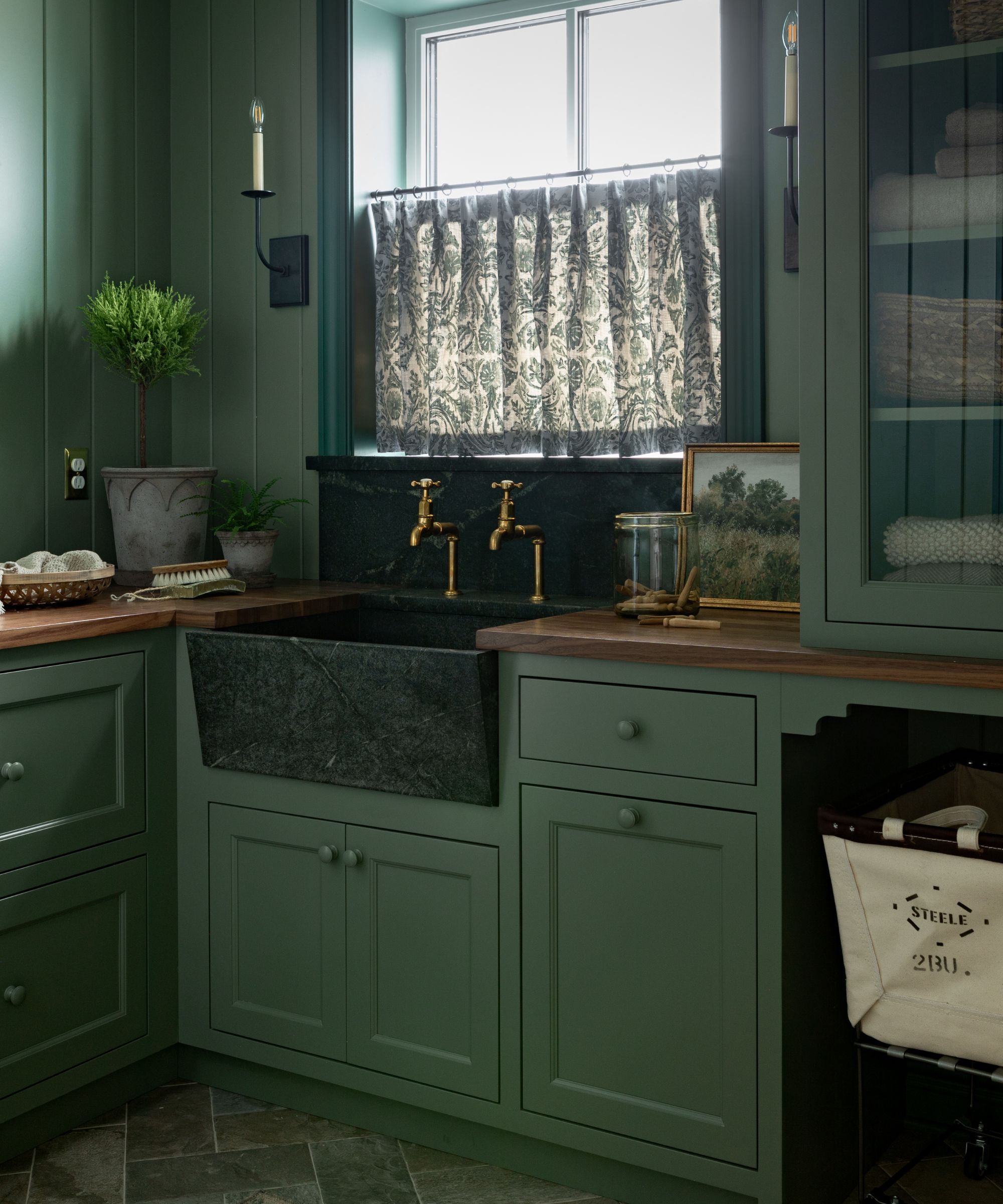 earthy green utility laundry room with color drenched walls and units, dark green marble sink and backsplash, and a small green floral cafe curtain