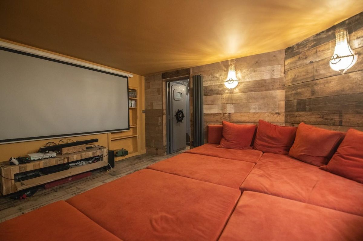 The home cinema has a large orange sofa and large black tv on the wall