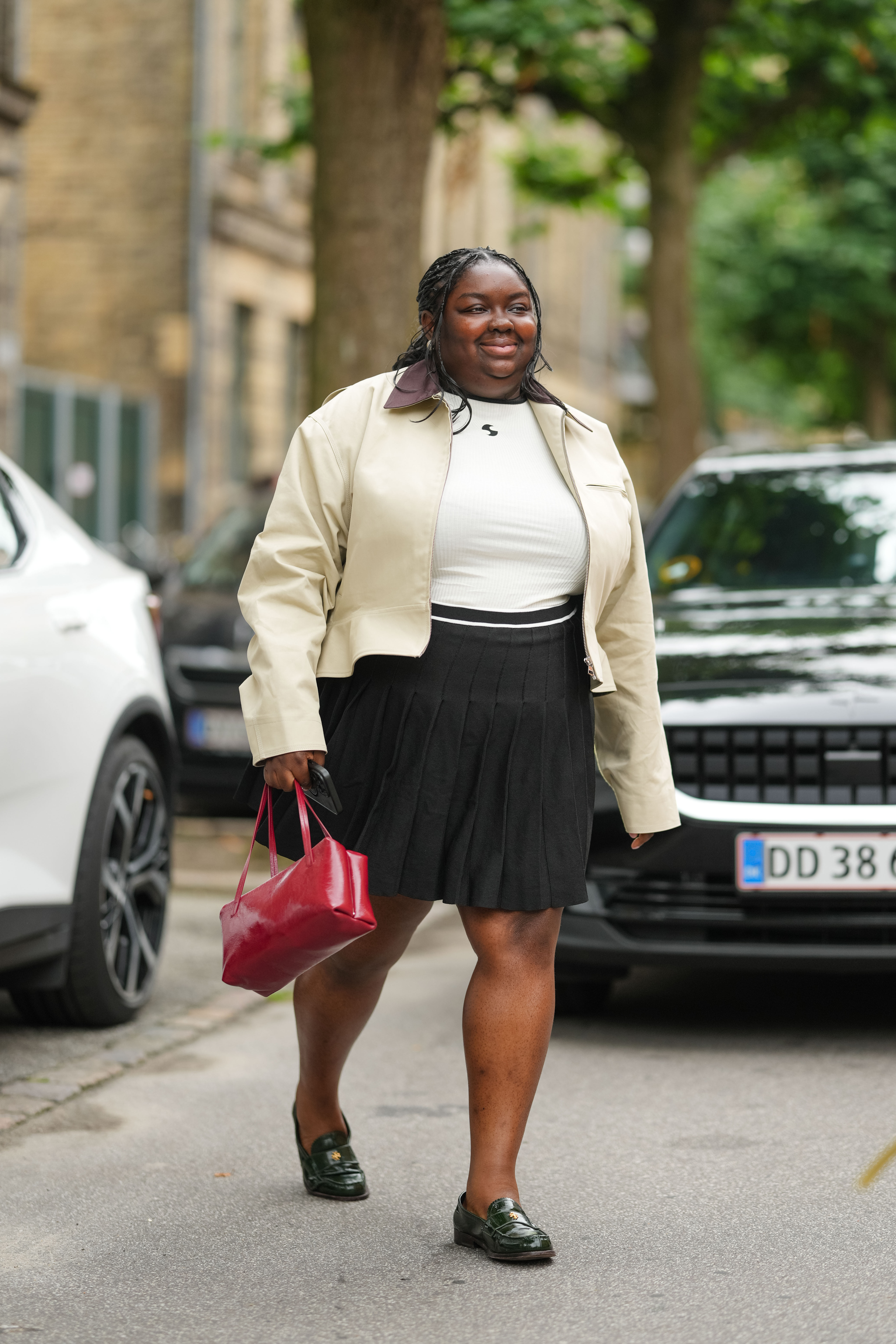 An image of @abimarvel wearing a country jacket from JW Anderson with a black pleated mini skirt and red Jil Sander bag while at the spring/summer 2026 season of Copenhagen Fashion Week.