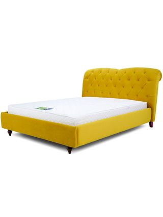 Yellow plush upholstered bed with Chesterfield-style buttoned headboard with mattress