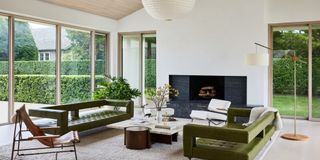 Japandi-style living room with large windows looking out on a lush backyard. The furniture inside is minimalist and low-slung, accented by paper lantern light fixtures