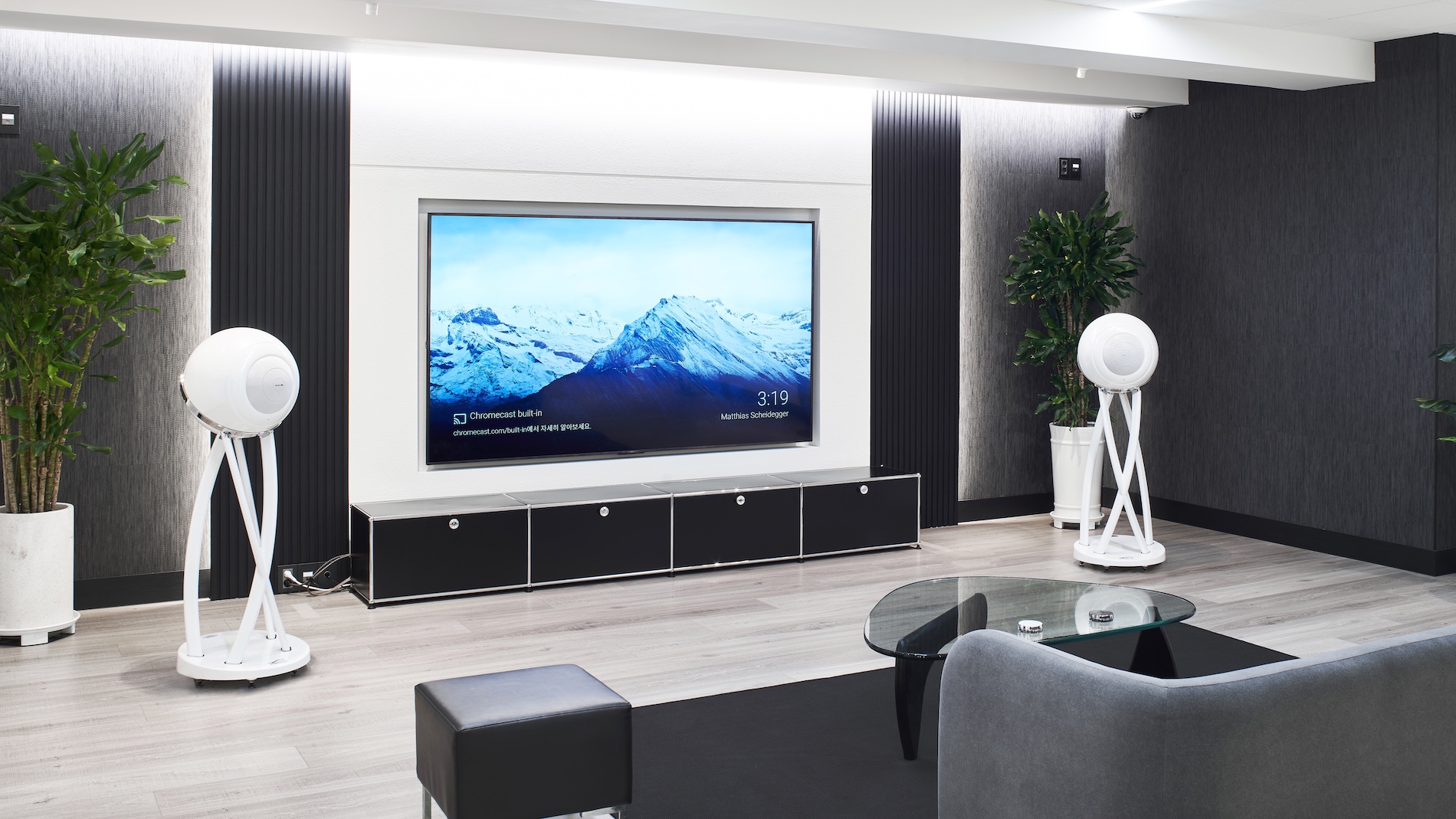 A pair of white floorstanding Cabasse speakers standing either side of a wall-mounted TV.,