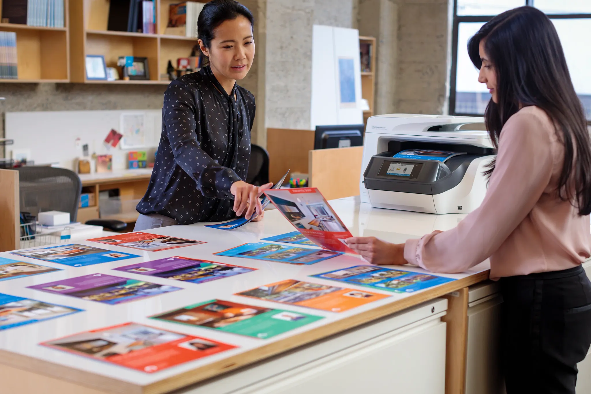 Two women standing next to a printer discussing design concepts