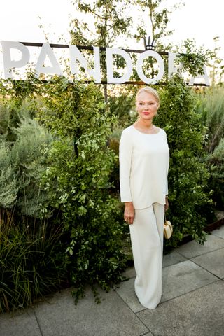 Pamela Anderson wears a white two-piece pant and long-sleeve set with a mini bag.