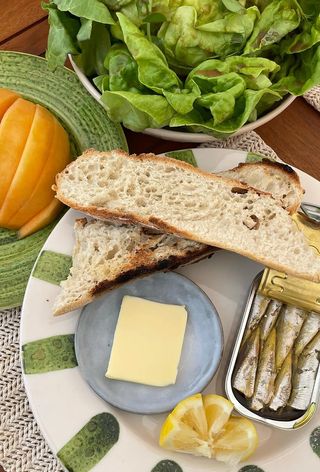 Plate with bread, sardines, butter, salad and melon