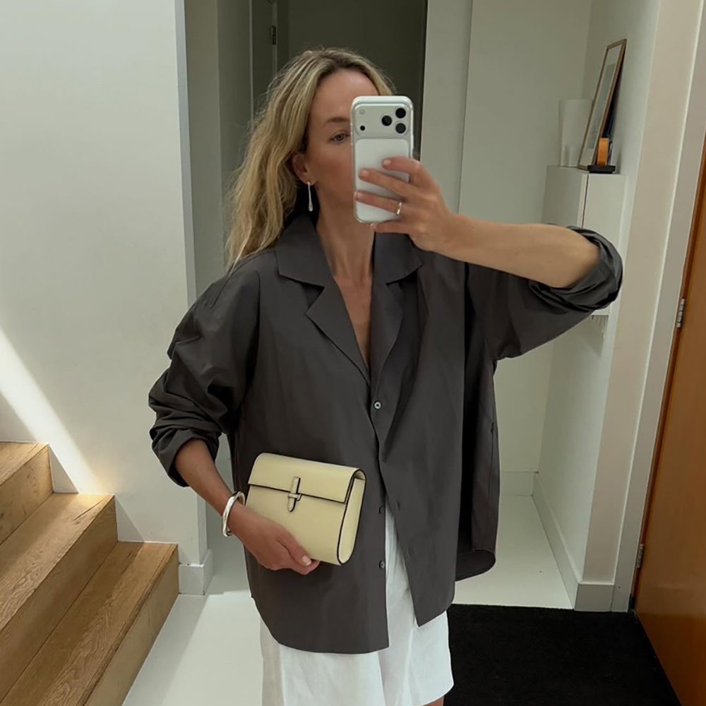 a woman wearing a dark gray button-down, white shorts, and butter yellow clutch