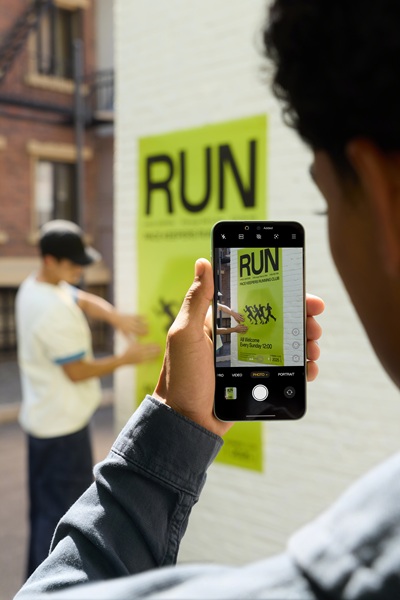 A model holding up the OnePlus 15R, using its camera to take a photo of a "RUN" poster.