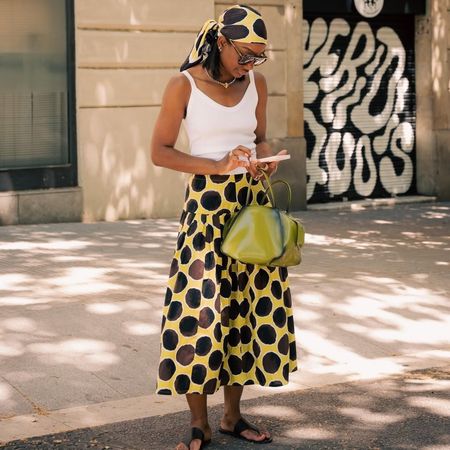 NYC woman wears a yellow and brown polka dot skirt with matching bandana and a white tank top.