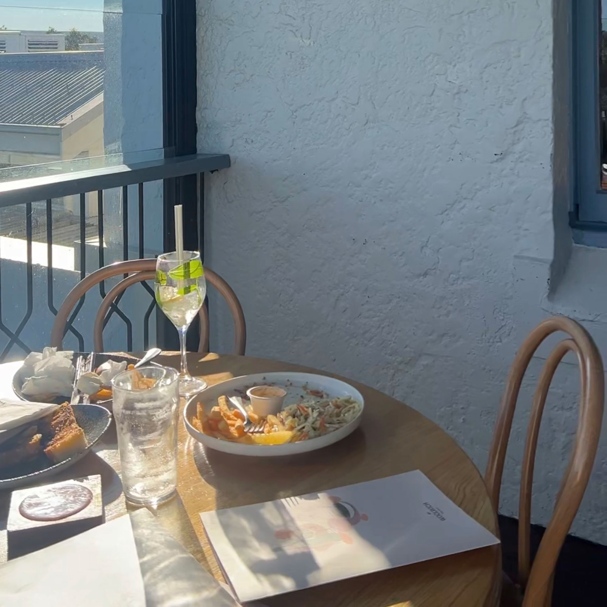 Round wooden table and matching chairs on balcony, with finished lunch dishes, drinks and menus