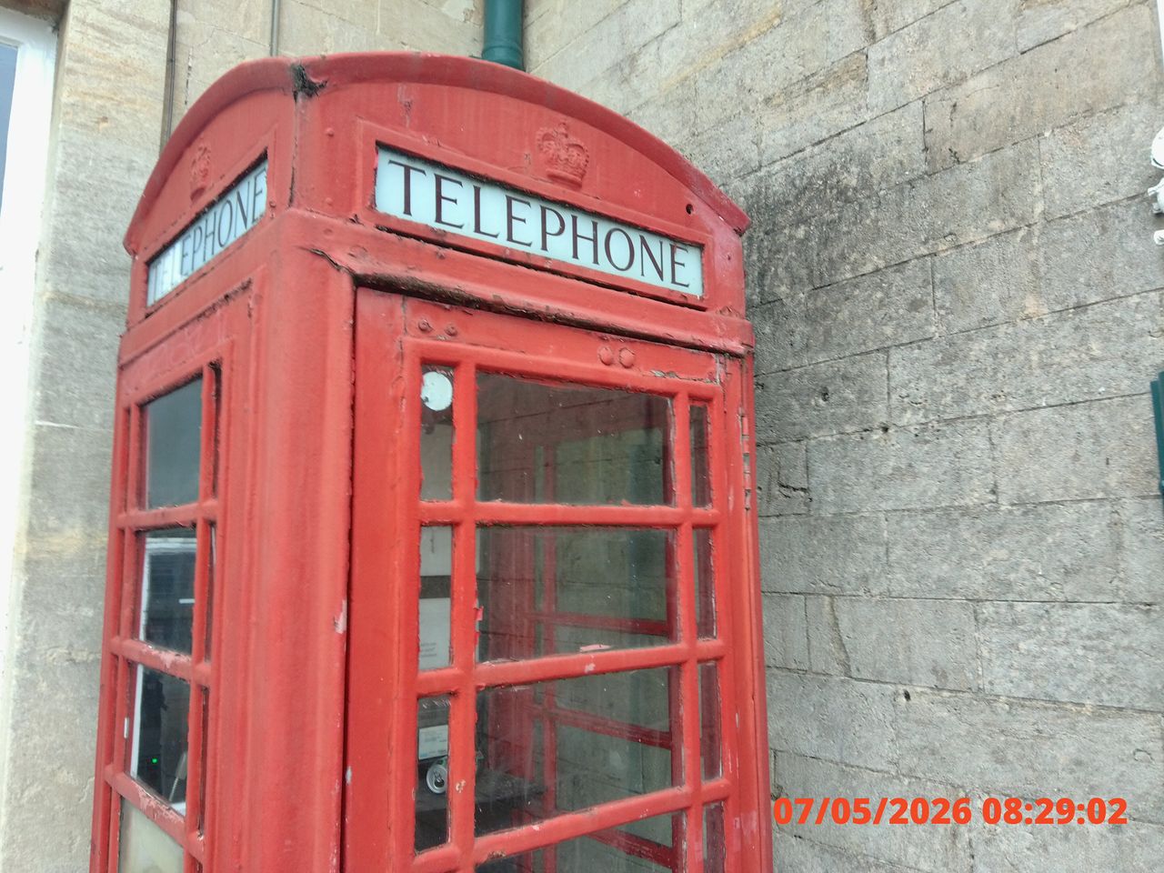 Red vintage telephone booth with worn paint set against a stone wall