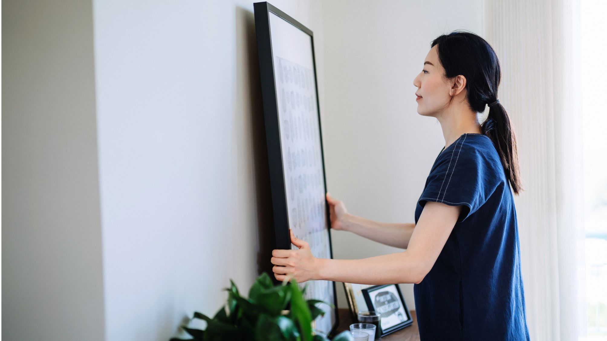 A woman hanging a new piece of art on her wall. 