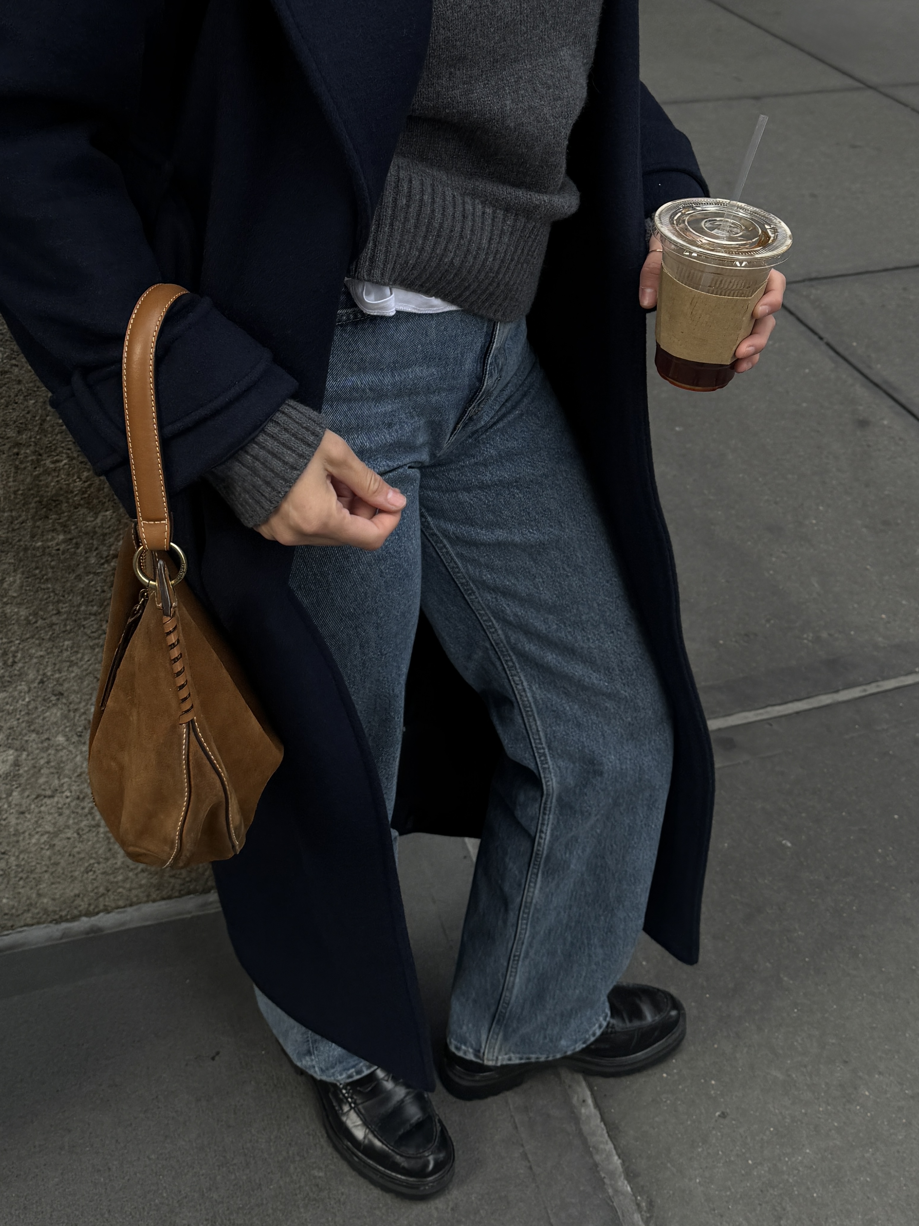 Kathryn Zahorak wearing black coat, navy sweater, loafers, and suede bag