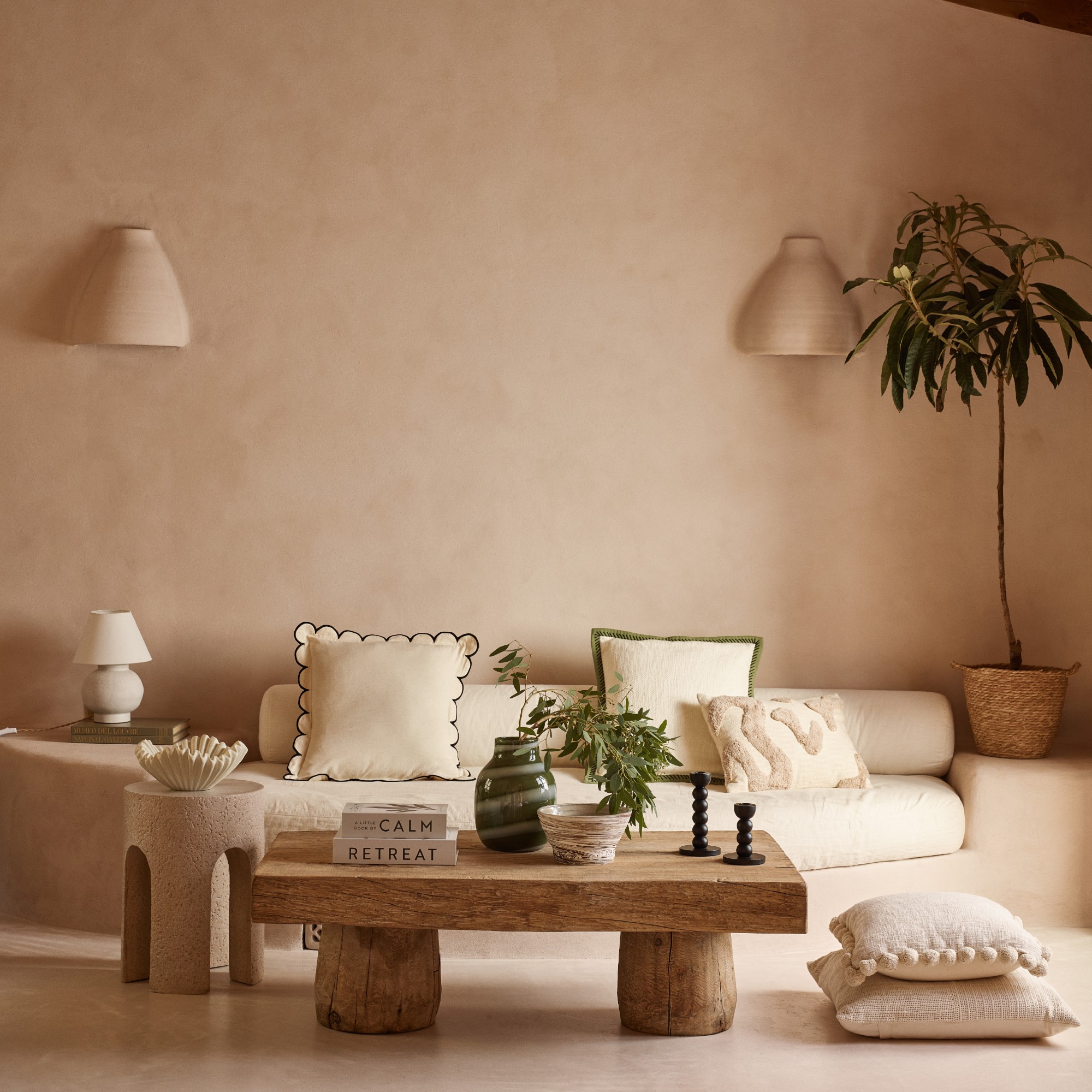 A limewash painted living room with built-in cream sofa decorated with George Home cushions, a wooden coffee table in front of it and a pleated bowl on a side table