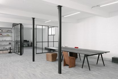 Interior view of the minimalist Studio Khachatryan featuring white walls, black pillars, large black table and brown chairs