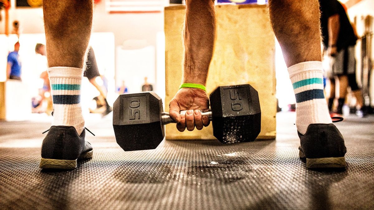 Close-up of hand holding dumbbell between person’s feet