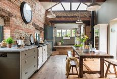 kitchen with high ceiling and beams and brick walls with green cabinets and old carved dark wood table with bench seats 