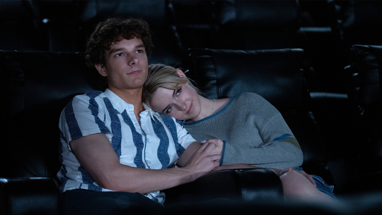 A teen couple (Mason Thames as Miller and Mckenna Grace as Clara) cuddle while sitting in a movie theater, in the romance movie 'Regretting You.'