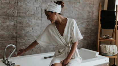 Young woman preparing a bath wearing a bathrobe