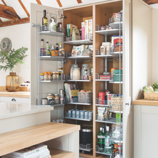 Large well stocked larder cupboard with doors open below vaulted ceiling with exposed beams. A kitchen project in a 19th century barn conversion, home to Jean and Stephen Field with three bedrooms in Canterbury, Kent.