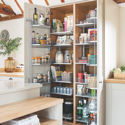 Large well stocked larder cupboard with doors open below vaulted ceiling with exposed beams. A kitchen project in a 19th century barn conversion, home to Jean and Stephen Field with three bedrooms in Canterbury, Kent.