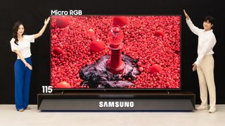 A man and a woman presenting the new Samsung 115-inch Micro RGB TV with a very bright red image on the screen