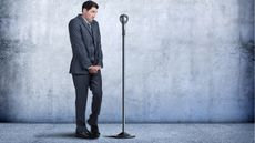 A guy in a business suit stands next to a microphone, looking shy and clearly wondering, How do you overcome stage fright?
