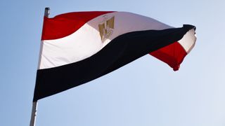 The Egyptian flag flying against a clear, pale blue sky