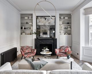 A white living room with pale grey alcove storage and sofa and colorful red armchairs.