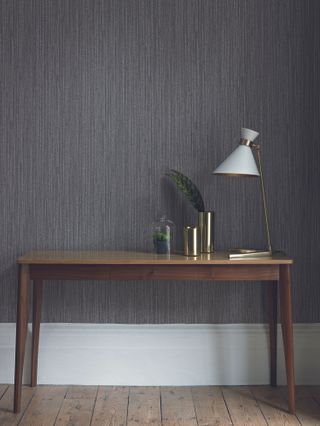A textured dark grey wallpaper wall covering in hallway with wooden table and white lampshade