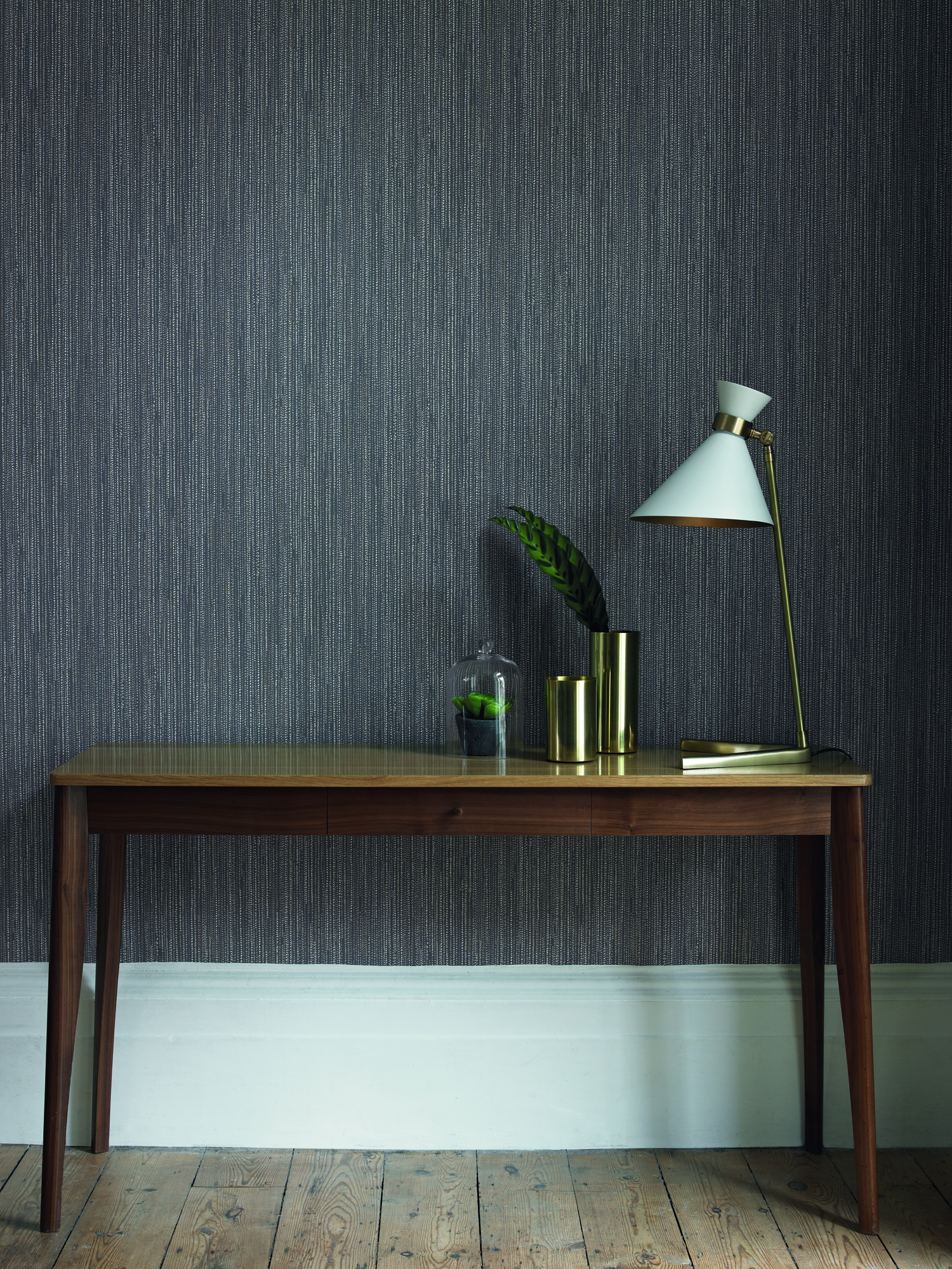 A textured dark grey wallpaper wall covering in hallway with wooden table and white lampshade