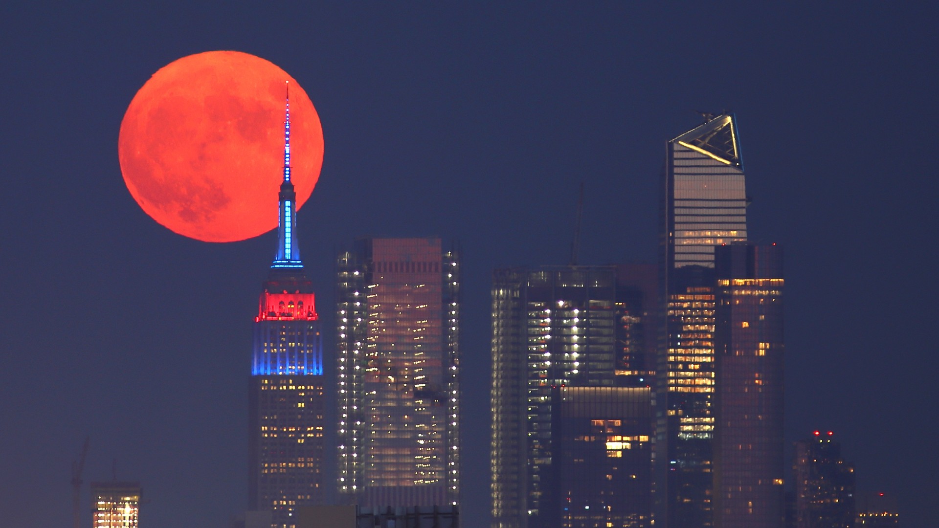 Une pleine lune Buck ou Thunder Moon (pleine lune rouge) est vue derrière Hudson Yards et l'Empire State Building dans les couleurs du drapeau des concurrents des Jeux olympiques de Tokyo vus de Lyndhurst le 23 juillet 2021 à New York.  , New Jersey.