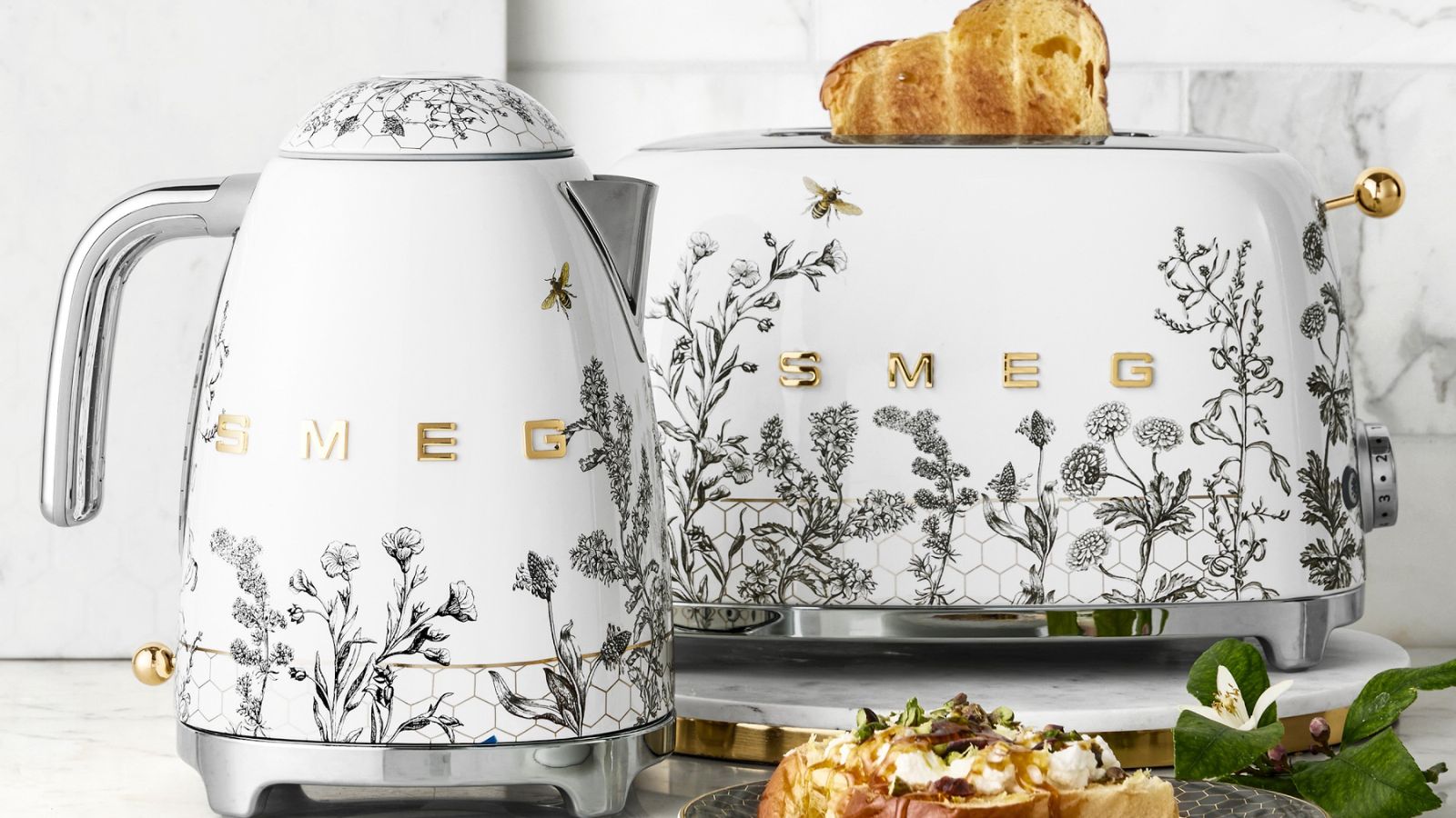 A SMEG kettle and toaster with grey flower and bee motifs on white bases, with stainless steel accents. 