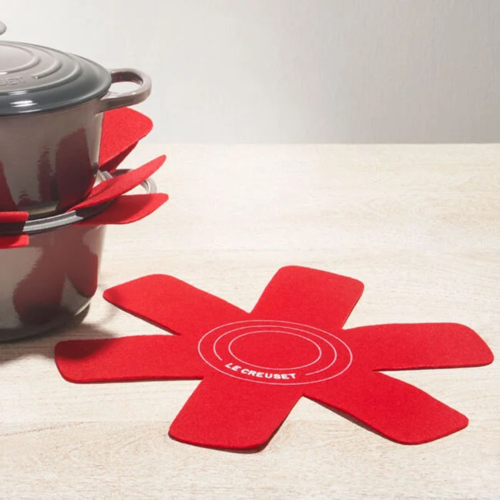 A red star shaped felt pan stacker protector, beside two stacked Dutch ovens with pan stackers visible inside.