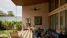 Image of a spacious covered outdoor patio. The exterior walls of the house are painted in a terracotta beige, and the flooring is a black and white diamond checkerboard. There is a seating area and a dining area on the patio, and the yard has lots of desert plants.