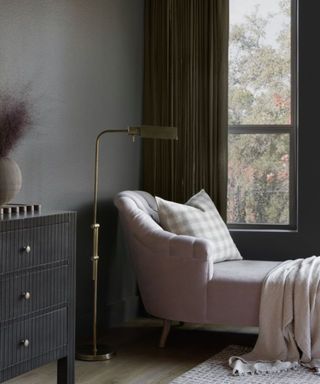 a corner of a room with grey walls, a pink chaise longue and a gold contemporary floor lamp