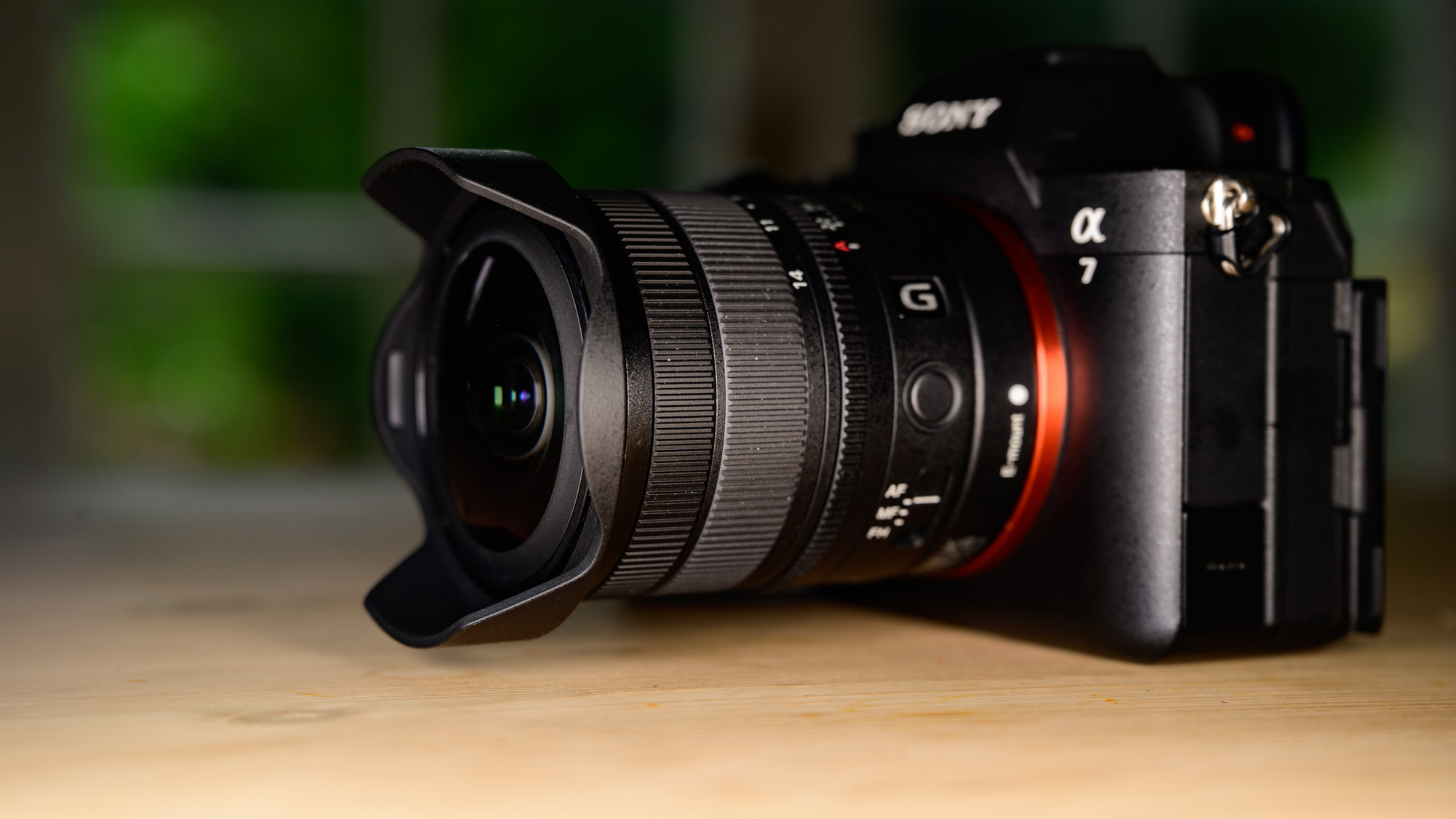 Sony FE 8-14mm F3.5 G fisheye lens attached to a Sony A7R V camera, on a wooden table, side profile