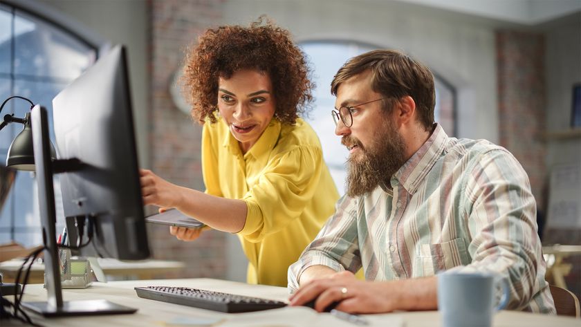 Staff onboarding concept image showing a female team member helping a new start in an open plan office space.