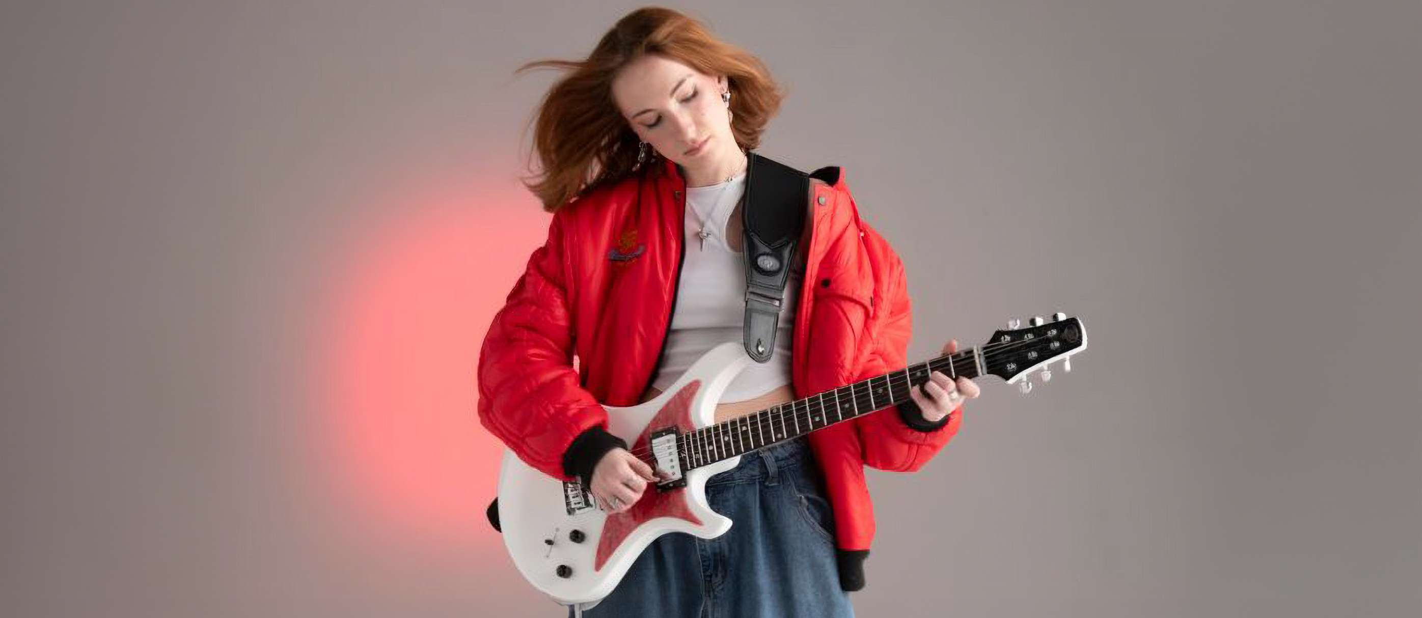 A photo of a woman playing a Venus Revolution guitar in white with a red pickguard