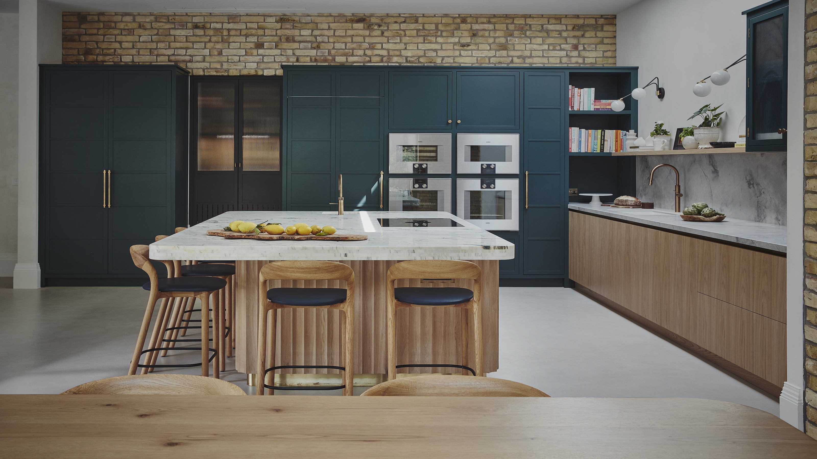 a bespoke kitchen showing a mix of handlefree cabinets on the island and base units and tall kitchen units in dark blue with gold handles and knobs
