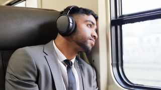 Man on train listening to pair of travel headphones