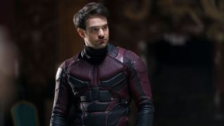 An unmasked Matt Murdock stands in a dark room with his Daredevil suit on in the character's Netflix series