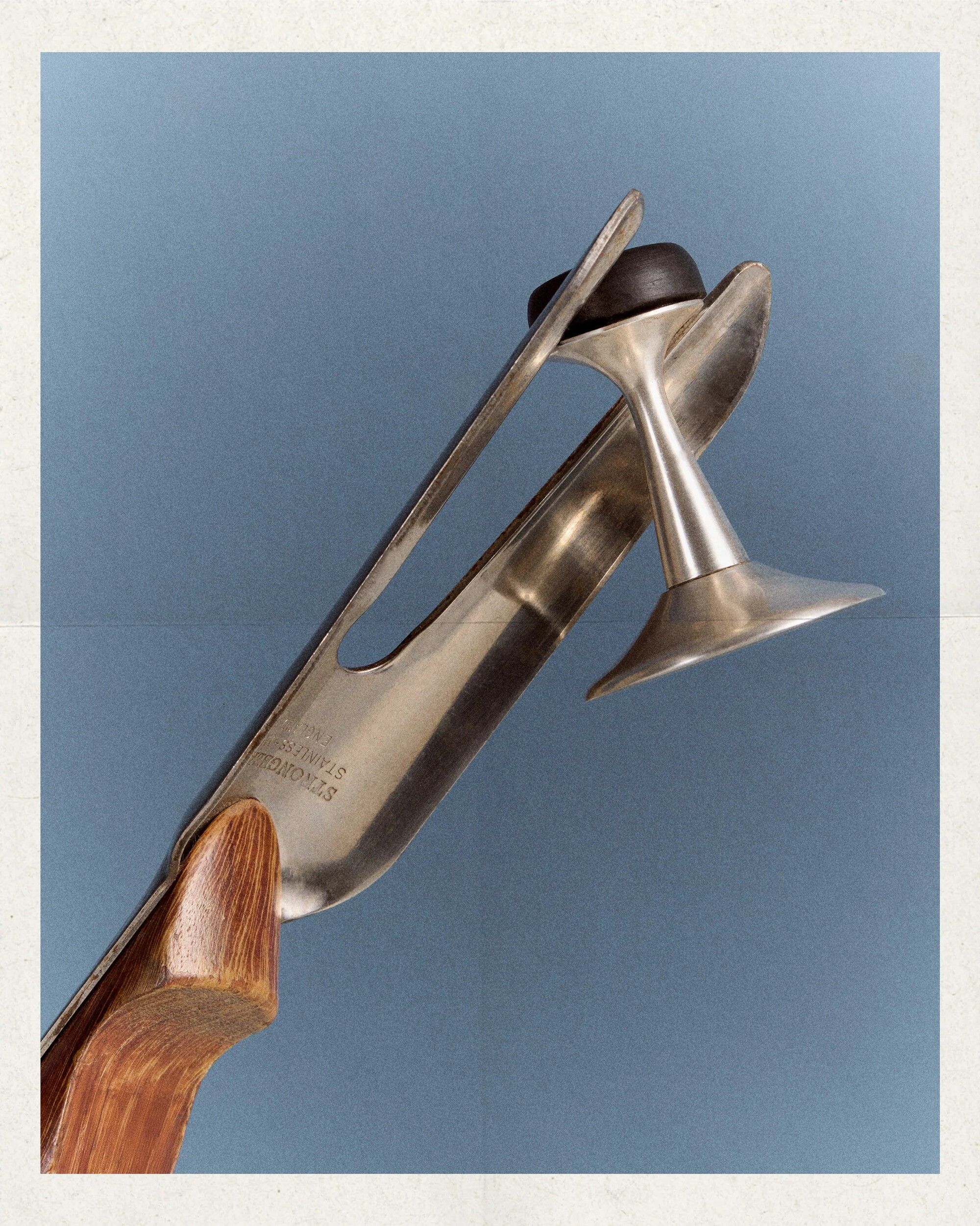 Image of a garden tool holding a silver doorstop in front of a blue background