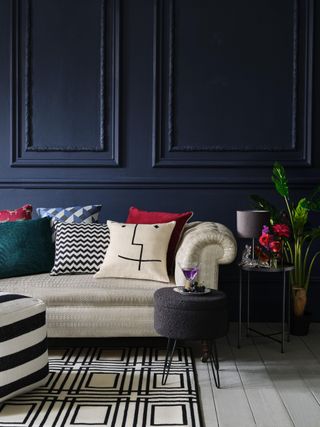 dark blue living room with panelling, cream sofa, monochromatic rug and footstool, white floors